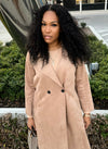 woman wearing e-curly bundles and matching e-curly frontal, wearing a tan coat standing outside in a parking lot in front of bushes