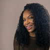 Woman with curly hair smiling against a beige background