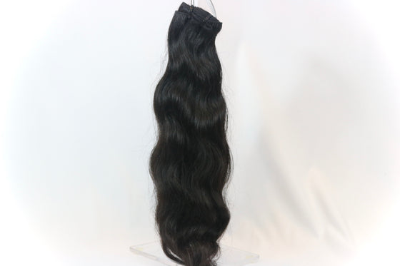 a bundle of black raw hair extensions in the wavy texture against a white surface