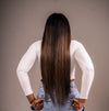A woman with long straight hair wearing a white top and blue jeans. She has long, straight, balayage colored hair that passes her waistline.