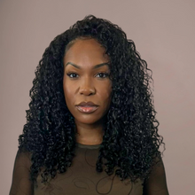  Woman with curly hair wearing a brown top against a beige background
