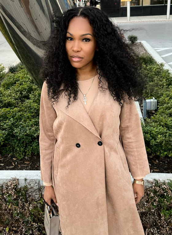 woman wearing e-curly bundles and matching e-curly frontal, wearing a tan coat standing outside in a parking lot in front of bushes