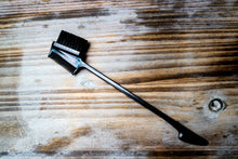  edge brush and small styling comb combo with glue applicator at the end laying on a wood surface