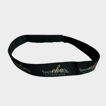  a black elastic hair band with the emerald hair extensions logo shown in a pattern displayed where the band is open in front of a white background.