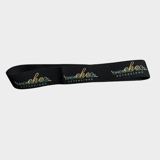 a black elastic hair band with the emerald hair extensions logo shown in a pattern with a white background