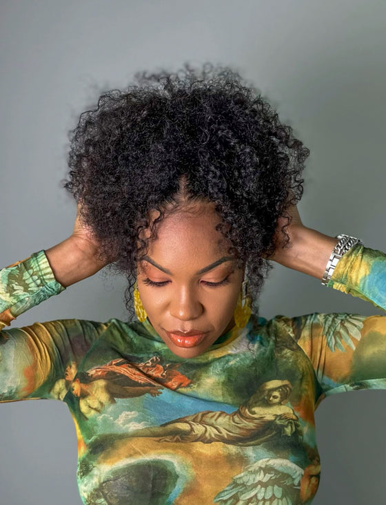 woman with kinky curly hair wearing a colorful, patterned shirt and accessorized with earrings.