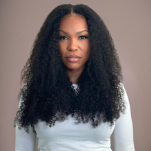  woman in kinky curly clip ins in a white top against a neutral background facing forward