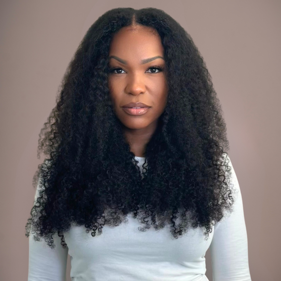 woman in kinky curly clip ins in a white top against a neutral background facing forward