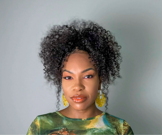 woman wearing kinky curly clip ins styled in a ponytail standing against a white background wearing a green top and matching accessories