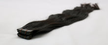  A bundle of wavy black tape-in hair extensions laid out on a white background.