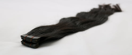 A bundle of wavy black tape-in hair extensions laid out on a white background.