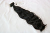 A bundle of wavy black tape-in hair extensions laid out on a white background.