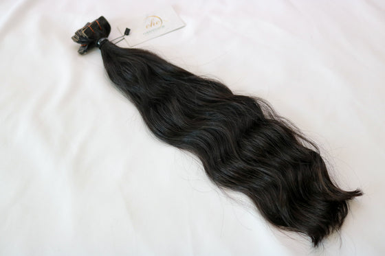A bundle of wavy black tape-in hair extensions laid out on a white background.