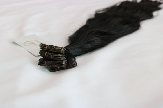 A bundle of wavy black tape-in hair extensions laid out on a white background.