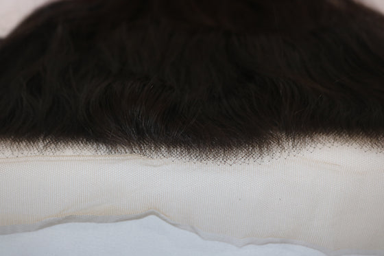 close up of transparent frontal lace in wavy texture laid against a white surface