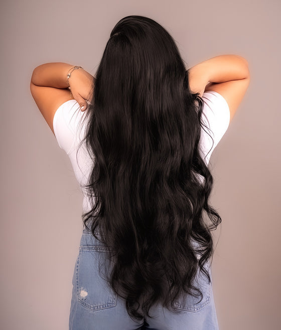 A woman with long wavy black hair wearing a white t-shirt and jeans, showcasing clip-in hair extensions.