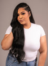 A woman with long wavy black hair wearing a white t-shirt and jeans, showcasing clip-in hair extensions.