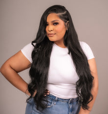  A woman with long wavy black hair wearing a white t-shirt and jeans, showcasing clip-in hair extensions.