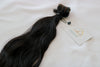 A bundle of wavy black tape-in hair extensions laid out on a white background.