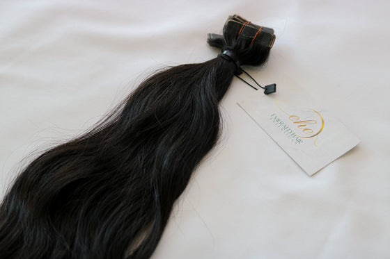 A bundle of wavy black tape-in hair extensions laid out on a white background.
